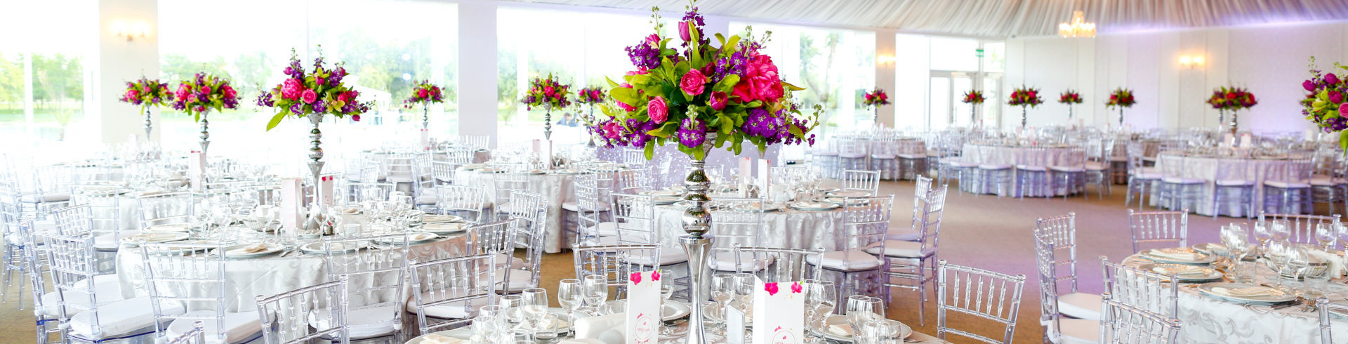 wedding reception hall decorated with beautiful floral centerpieces and clear ghost chairs